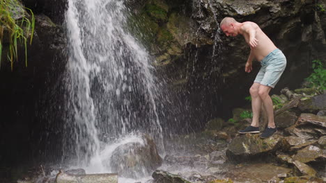 tourist wets bald head with waterfall streams at highland