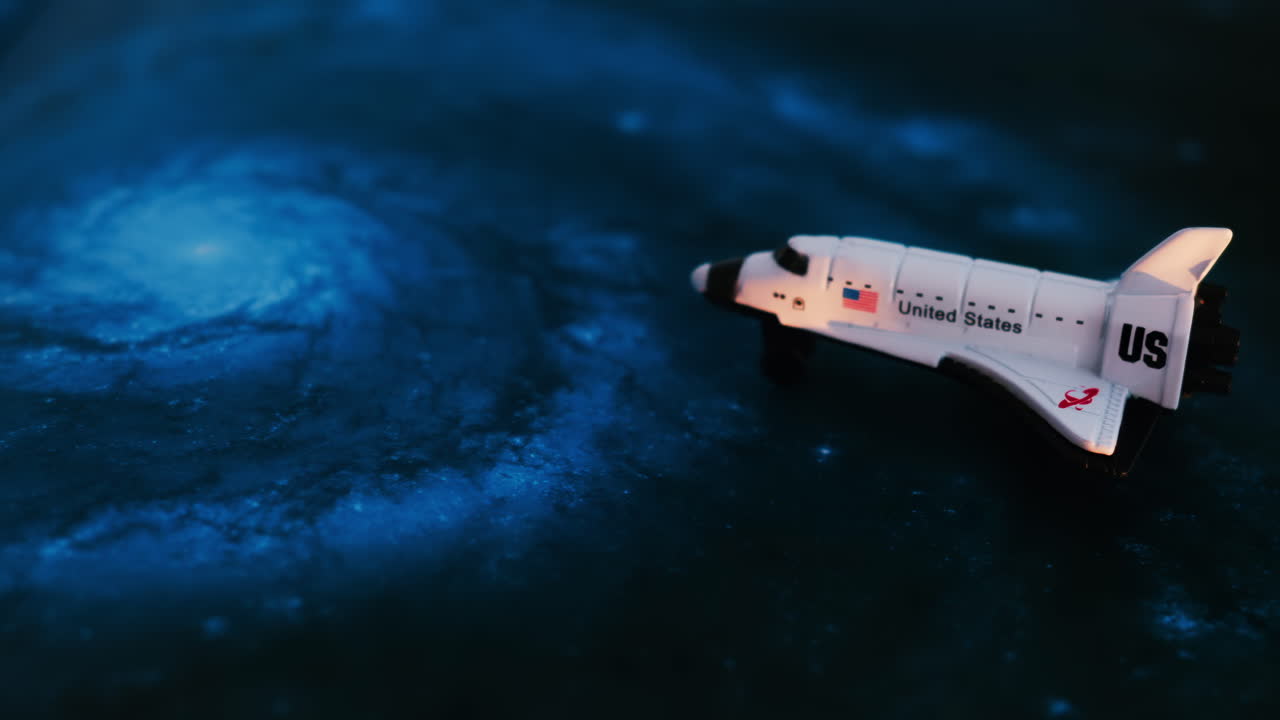 Close up of a miniature toy space shuttle placed on a blue cosmic galaxy backdrop