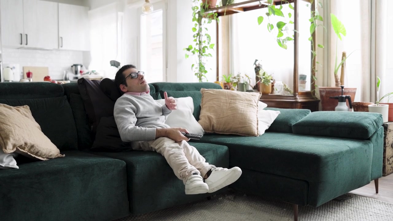 Young Man Relaxing on Green Sofa Watching Television at Home