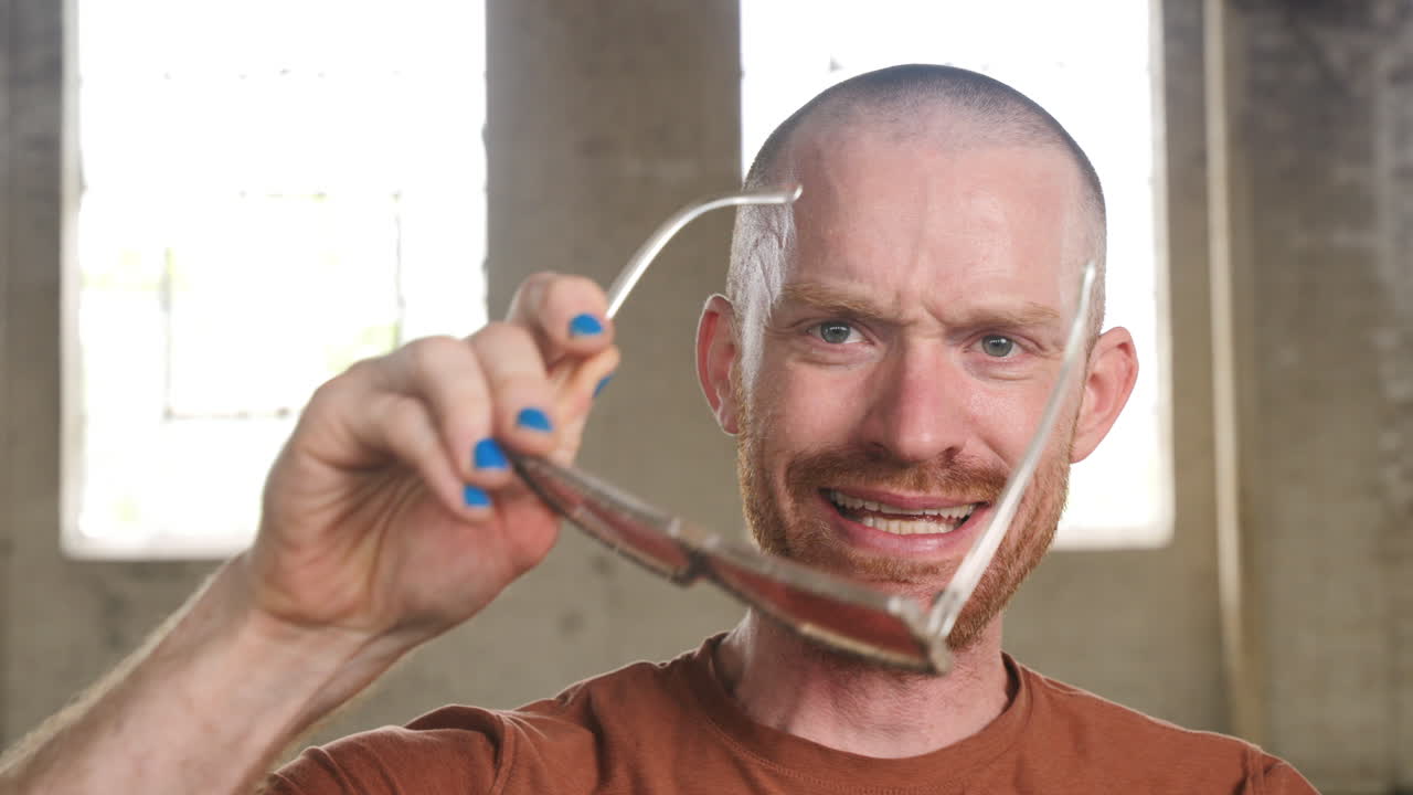 Slow motion footage of a man in an industrial warehouse setting talking into camera and putting on rose colored glasses.