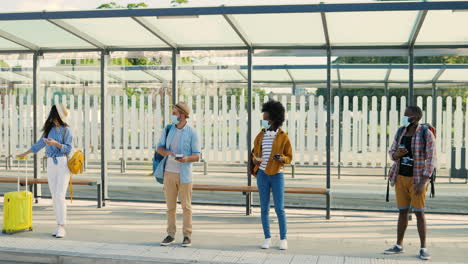 multiethnic young males and females travellers in medical masks waiting for transport at bus stop