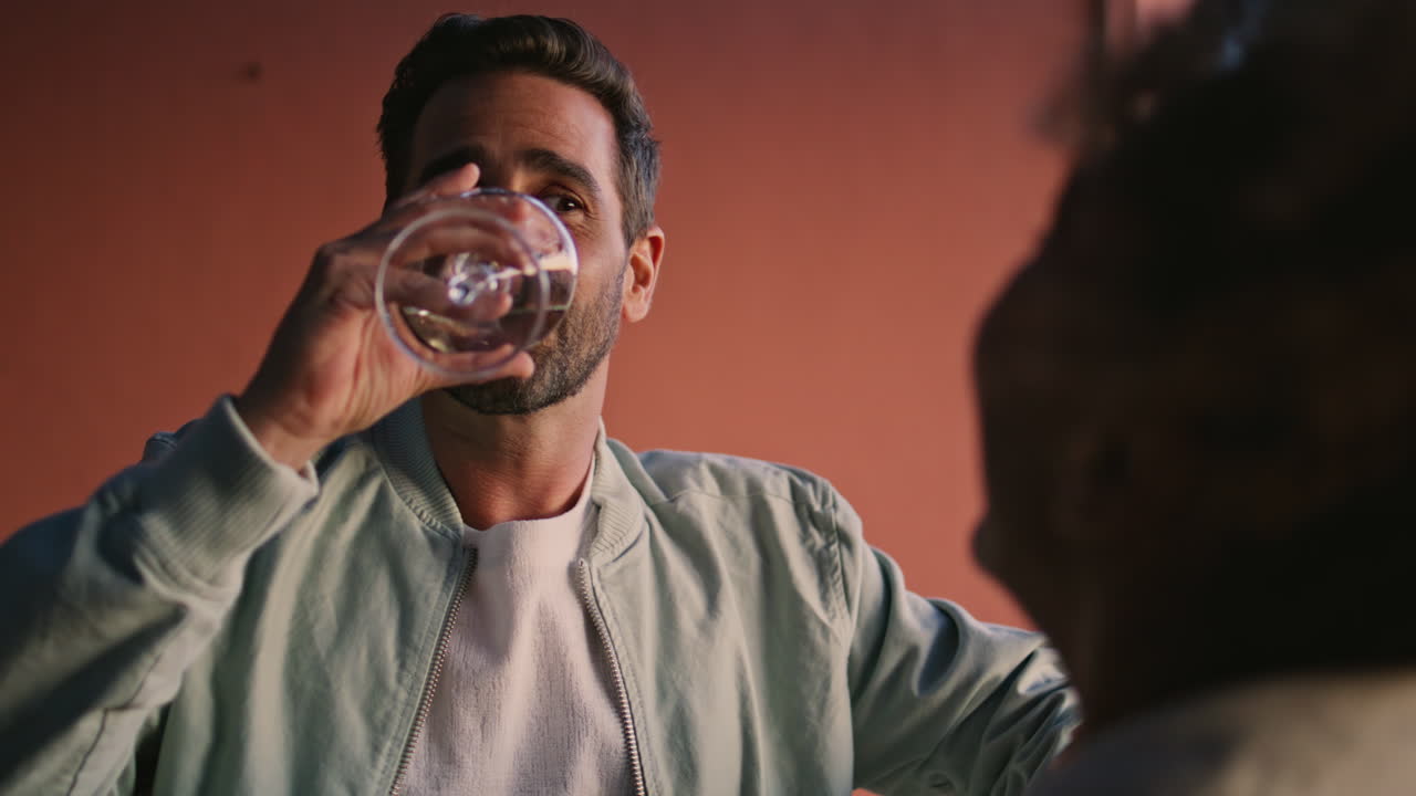 쾌활한 남자가 해가 지는 저녁에 발코니에서 여자와 얘기하고 친구들이 웃고 있다.