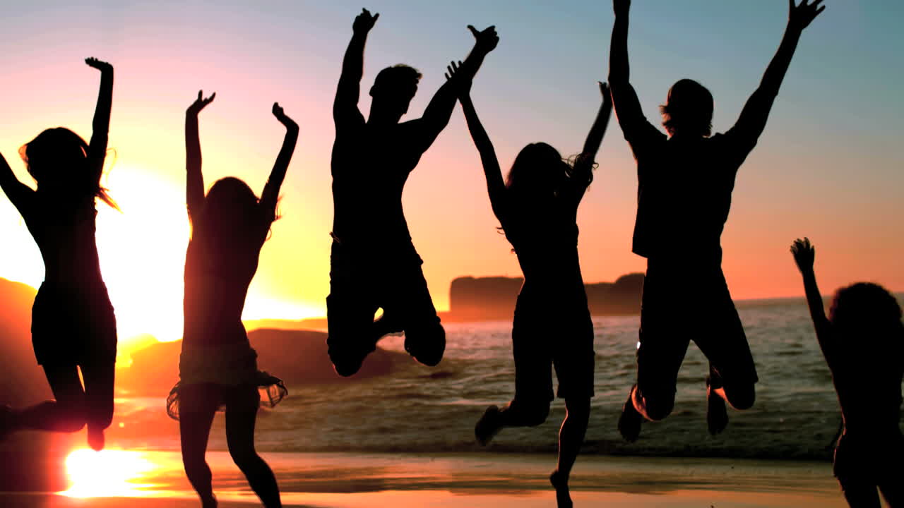 Group of friends jumping on the beach under the dusk