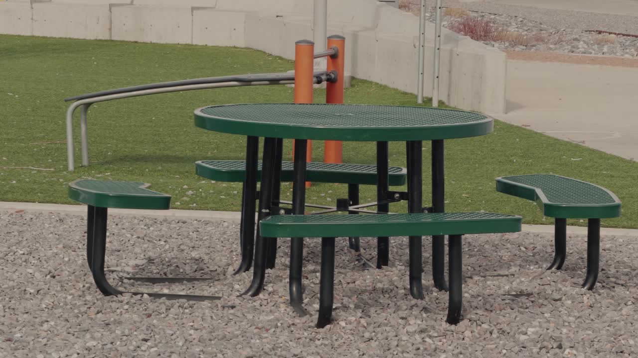 Slow steady pan of empty picnic table on gravel beside grass recreation area