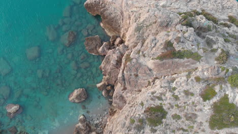 Un-Dron-Captura-El-Ojo-De-Un-Pájaro-En-El-Borde-Rocoso-De-Un-Acantilado,-Mientras-La-Cámara-Se-Eleva-Sobre-Un-Paisaje-Escarpado-De-Agua-Azul-Y-Paredes-De-Piedra-Blanca