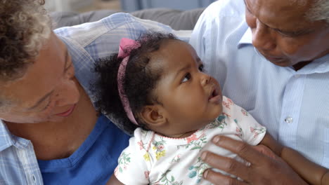 Grandparents-Sitting-On-Sofa-At-Home-With-Baby-Granddaughter