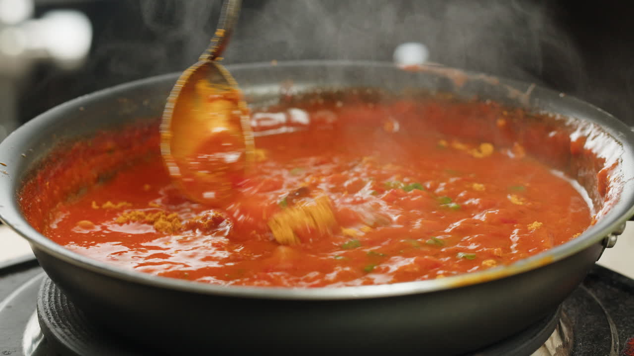 Chicken in tomato sauce is boiling on a frying pan with spices. Cooking tomato sauce curry with chicken fillet. Traditional Italian Mexican Asian dish. High quality studio shot for cafe, restaurant close up.