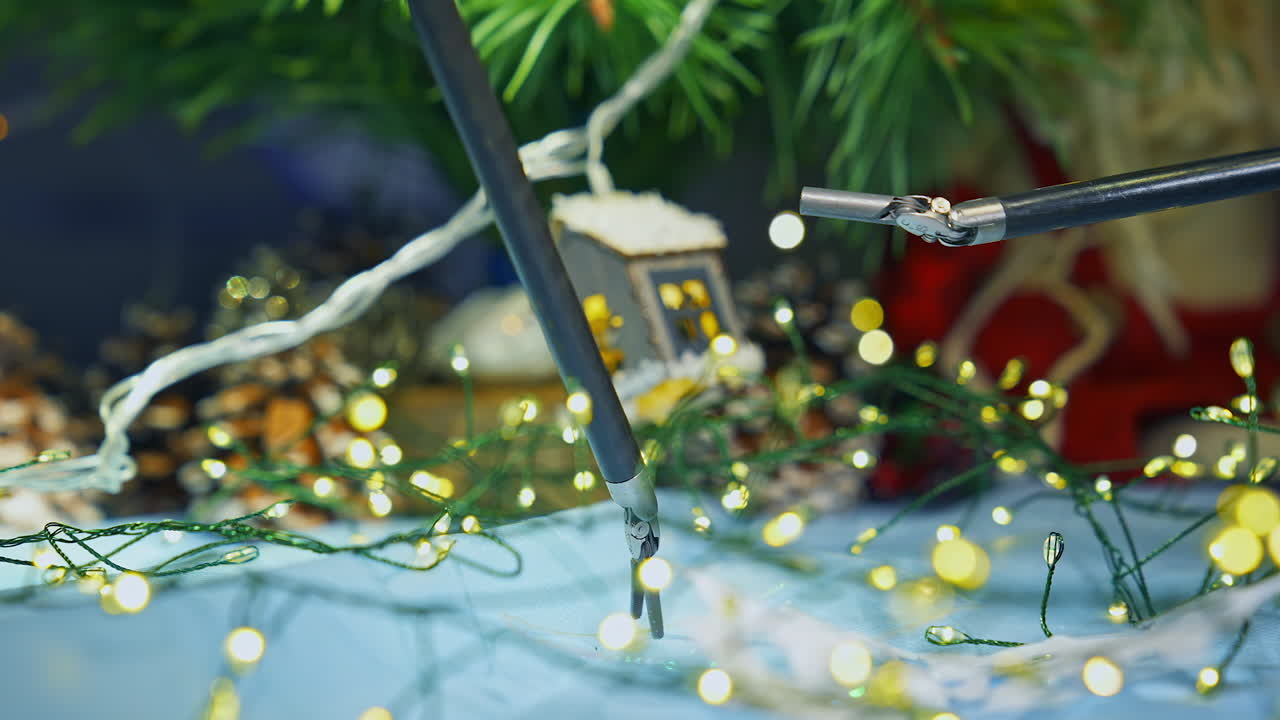 Two manipulators of high-precision surgery technology hold the wires from decoration lights. Precise movements of robotic arms. Christmas tree and decorations at the backdrop.