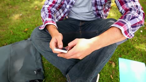 estudiante sentado en el césped enviando mensajes de texto por teléfono