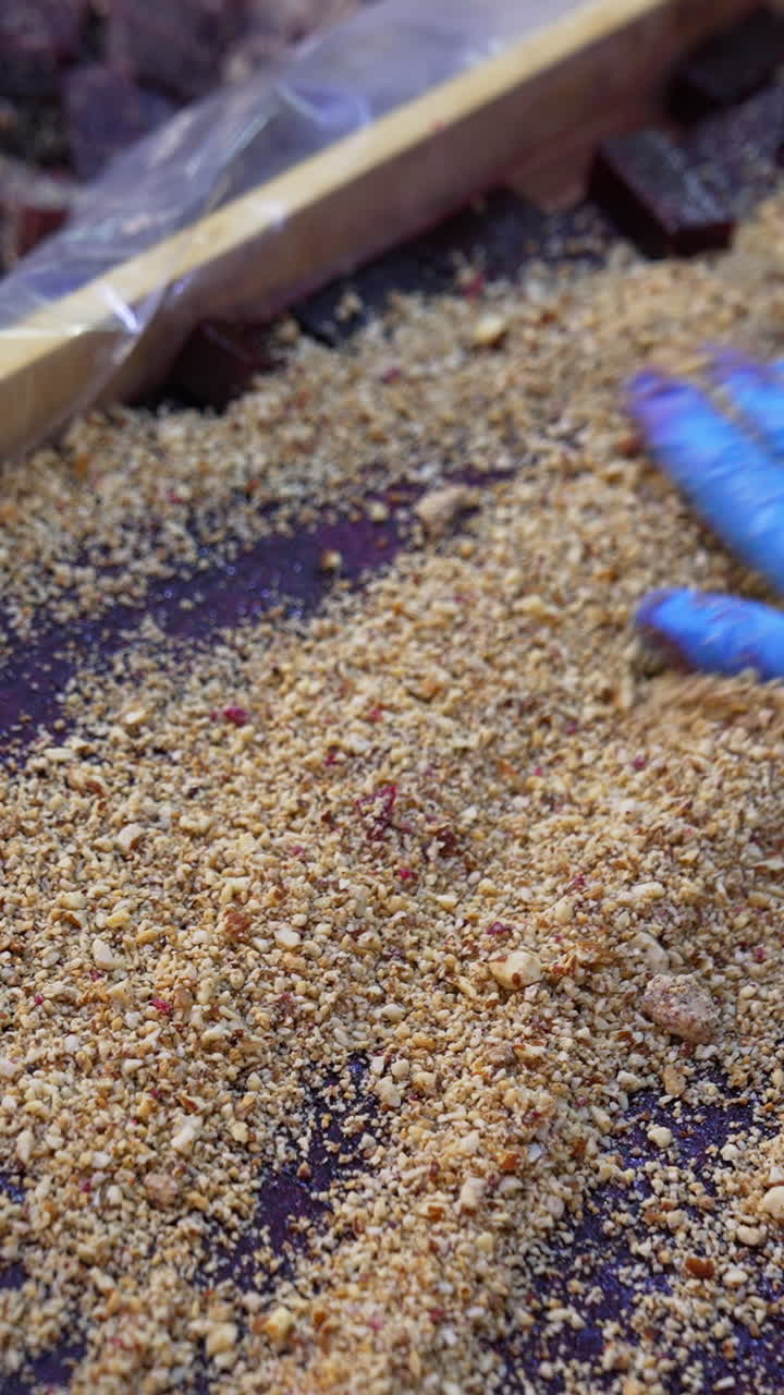 Purple dark layer of marmalade cut into pieces in a wooden box. Worker spreads nuts over the sweet candied fruit jelly. Close up. Vertical video