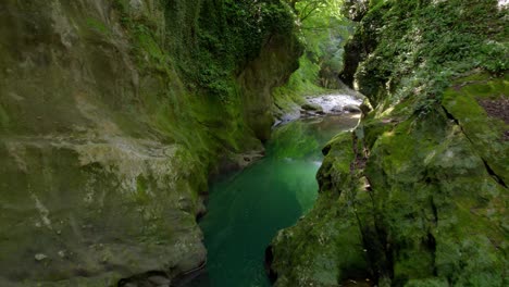 A-drone-flies-through-a-lush-Georgian-canyon,-showcasing-cliffs,-water,-and-greenery