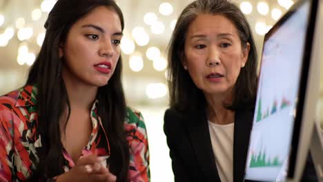 two professional women analyzing data together in a collaborative environment while engaging in insightful conversation and reviewing graphs on a computer screen