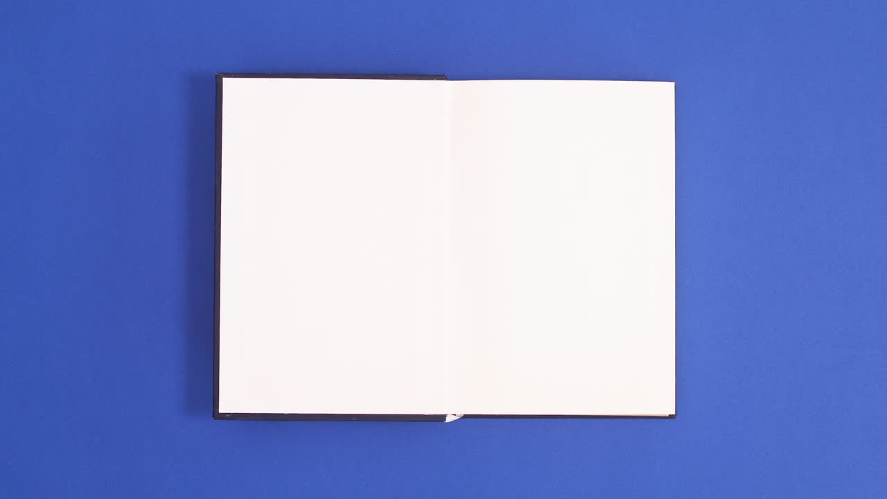 Dark Blue vintage hardcover book appear and open with copy space on blue background. Stop motion flat lay