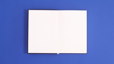 dark blue vintage hardcover book appear and open with copy space on blue background. stop motion flat lay