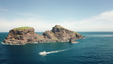 White-yacht-exploring-remote-coastline-of-Ilhéu-do-Farol-in-Madeira,-aerial