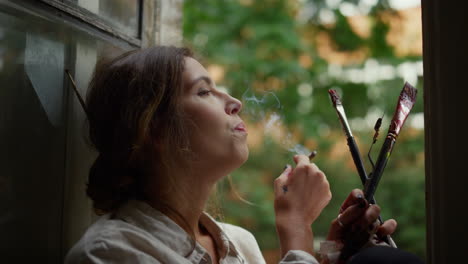 Creative-woman-holding-cigarette-indoors.-Female-painter-smoking-on-windowsill.