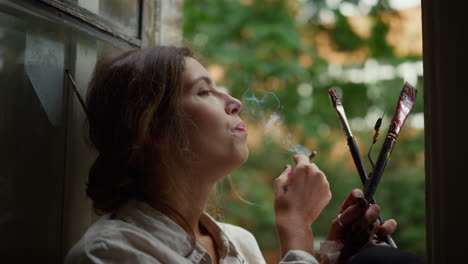 una mujer creativa con un cigarrillo en el interior, una pintora fumando en el alféizar de la ventana.
