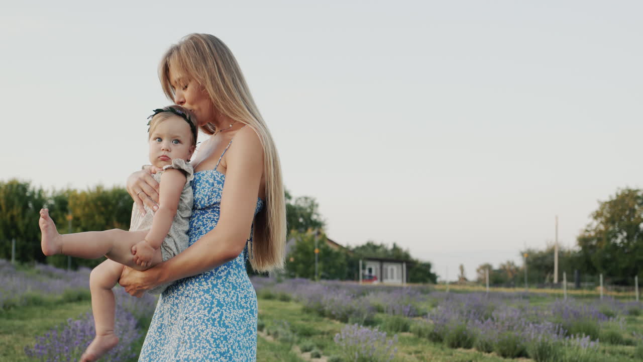 madre atractiva de cabello largo sostiene a su pequeña hija en sus brazos. de pie en un campo de lavanda en flor