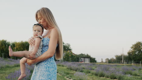 attractive mother with long hair holds her little daughter in her arms. standing in a field of blooming lavender