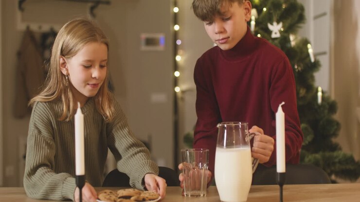A Blond Boy And His Blond Sister Place An Empty Glass, A Jug Of Milk And A Plate Full Of Cookies On An Empty Table With Two Candles, Then They Leave The Room 1