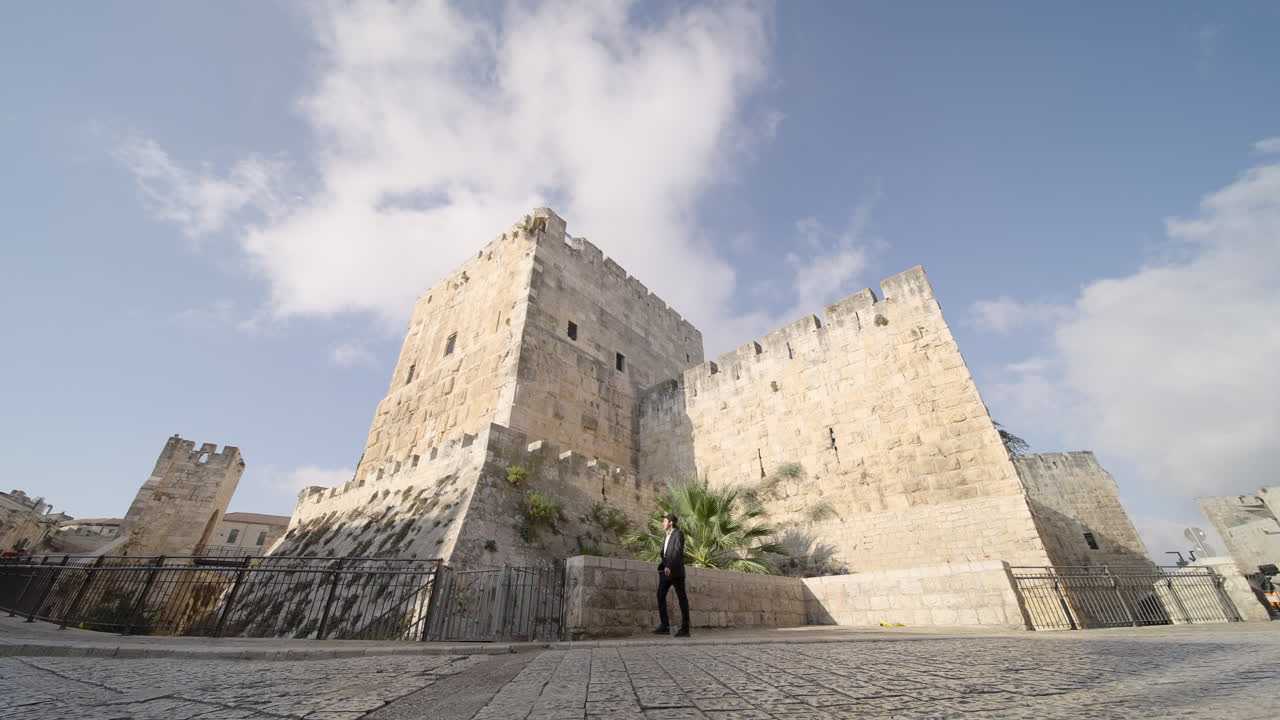 Wide angle shot of a young model in black suit and hat loitering around an old city of david in Jerusalem during daytime