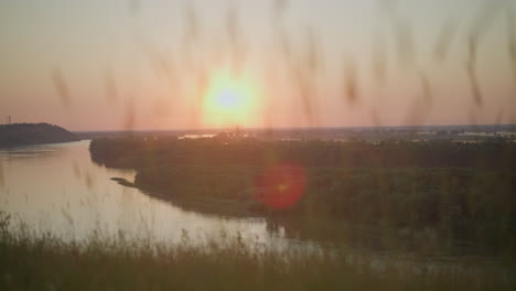 a tranquil scene of a peaceful lake surrounded by lush greenery, with tall grasses gently swaying in the foreground as the sun sets, casting warm, golden light across the serene landscape