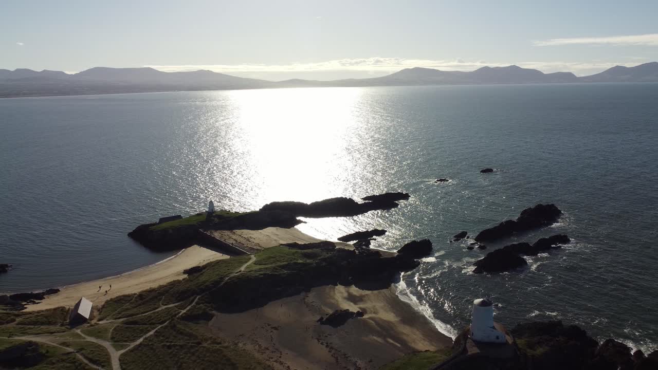 vista aérea de reversión sobre la isla galesa de ynys llanddwyn con el océano brillante y la cordillera nebulosa de snowdonia a través del horizonte del amanecer