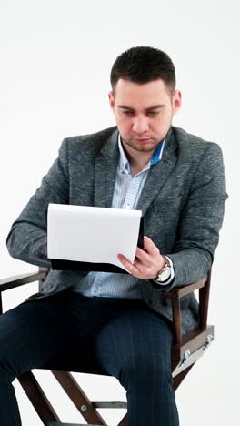 handsome businessman reading documents. young man in grey suit sitting on a wooden chair and looking the paperworks on white background. vertical video