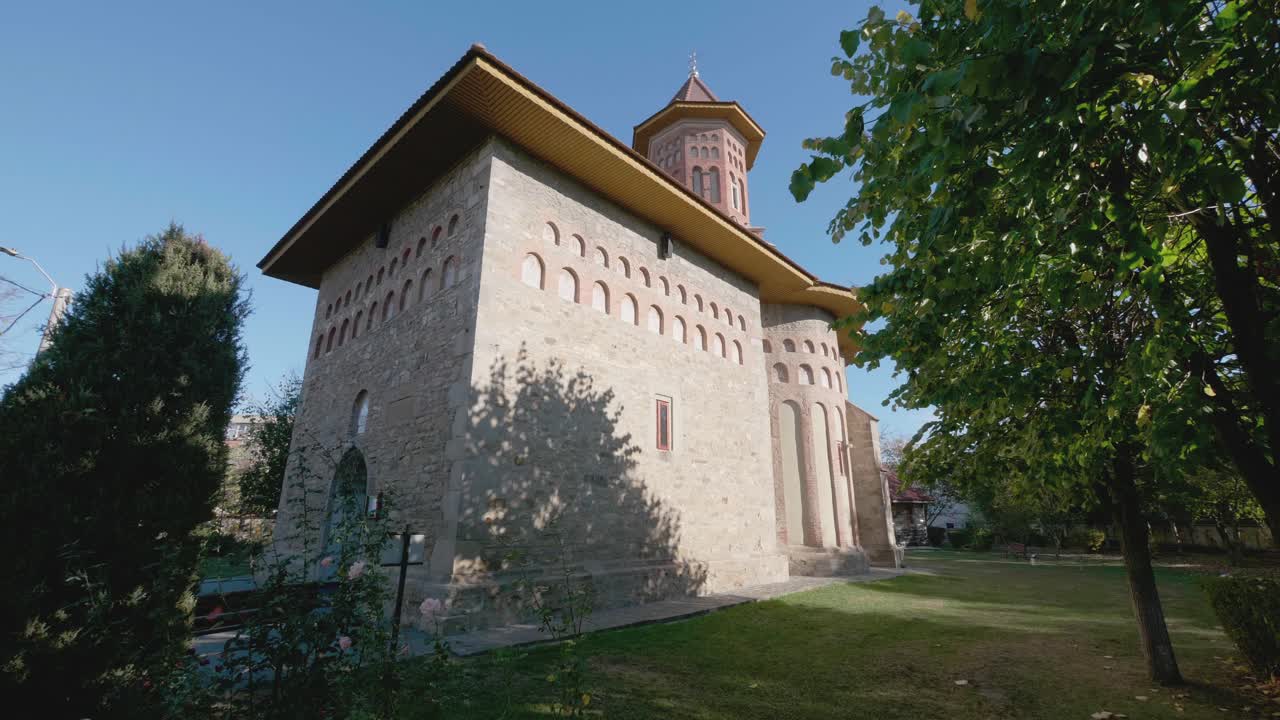 A static shot of the historic Precista Church in Bacau, Romania. The 15th-century medieval Orthodox landmark is surrounded by green trees on a sunny summer day