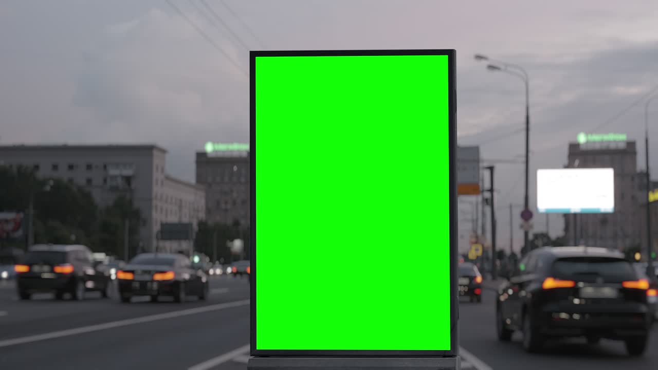Cartellone pubblicitario con schermo verde su un'autostrada trafficata con traffico, luci al neon