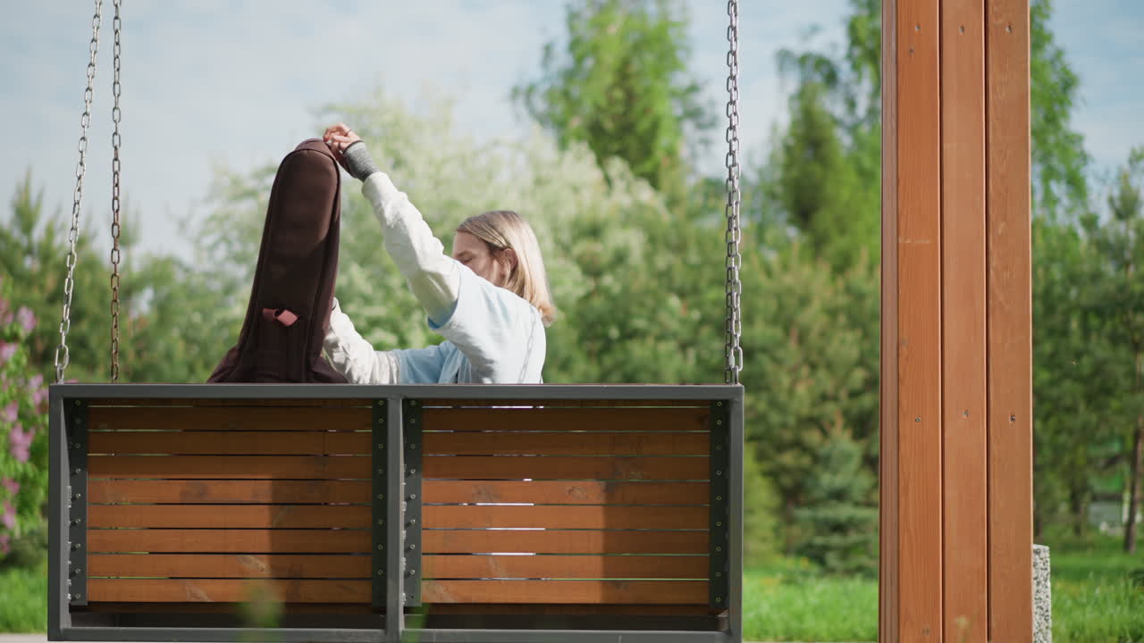 Vaalea, valkotukkainen nainen kitarakoteloineen puutarhakeinussa aurinkoisessa puutarhassa, avaa kotelon, nostaa akustisen kitaran, hellii soitinta, virittää kieliä, nojaa taaksepäin silmät suljettuina, rauhallinen cottagecore-tunnelma, intiimi
