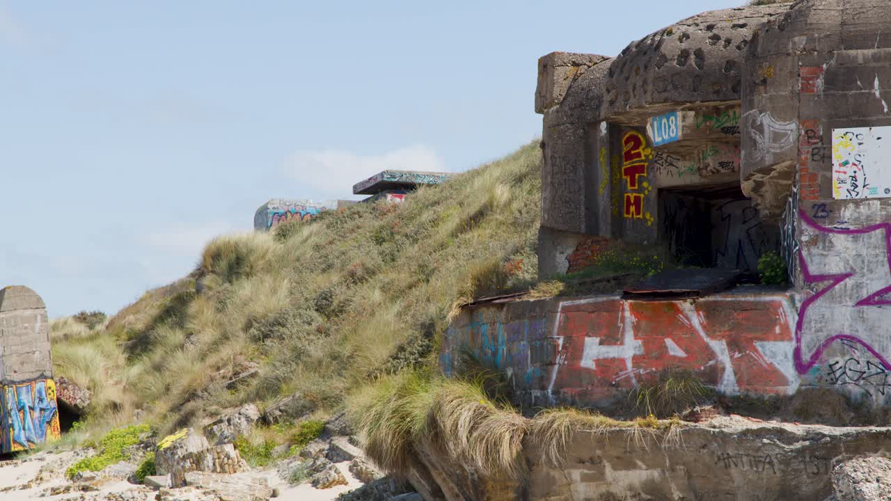Static daylight shot of historic concrete bunker with graffiti, sandy dunes, and blue sky background