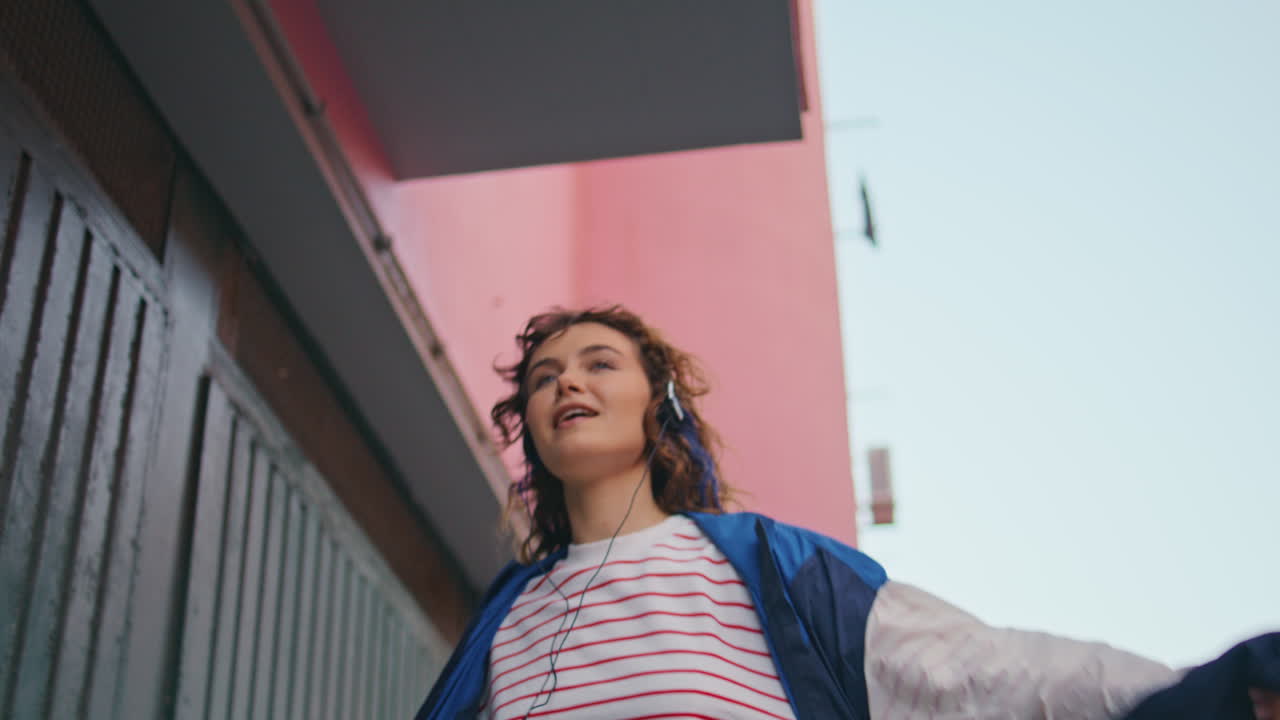 mujer divertida con auriculares bailando en la calle cantando su canción favorita de cerca.