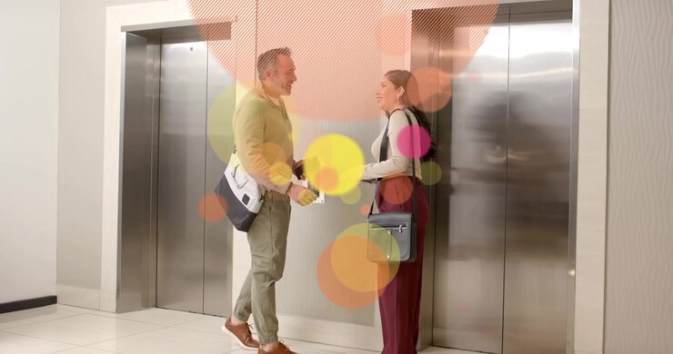 Kontorduo går mod elevatoren, kvinde trykker på kaldeknap, og deler en tablet til arbejde, mens bobler vokser frem