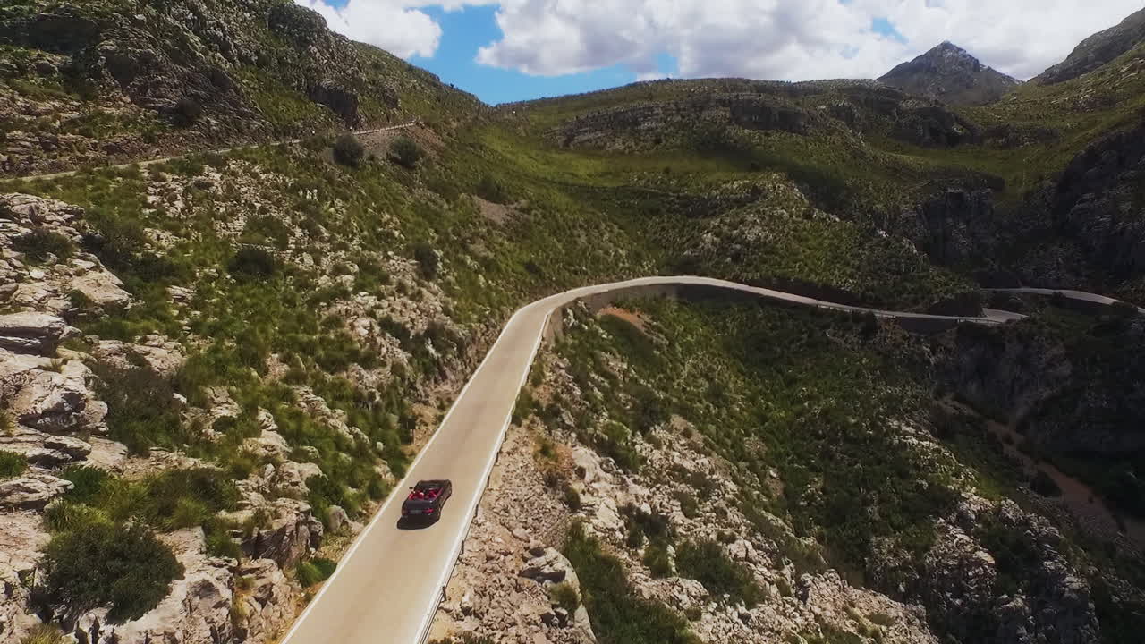 Un dron sigue a un descapotable por carreteras sinuosas y luego se detiene cuando el coche se aleja.