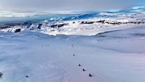 Vista-Aérea-Del-Paisaje-Sobre-Personas-Que-Viajan-En-Motos-De-Nieve-En-El-Suelo-Helado-Del-Glaciar-Myrdalsjokull-En-Islandia,-Al-Atardecer