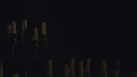 a group of white candles some on a candelabra lit up then blown out by a strong wind