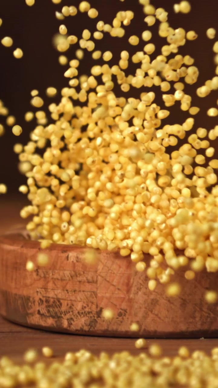 Grani di miglio che cadono in una ciotola di legno al rallentatore.