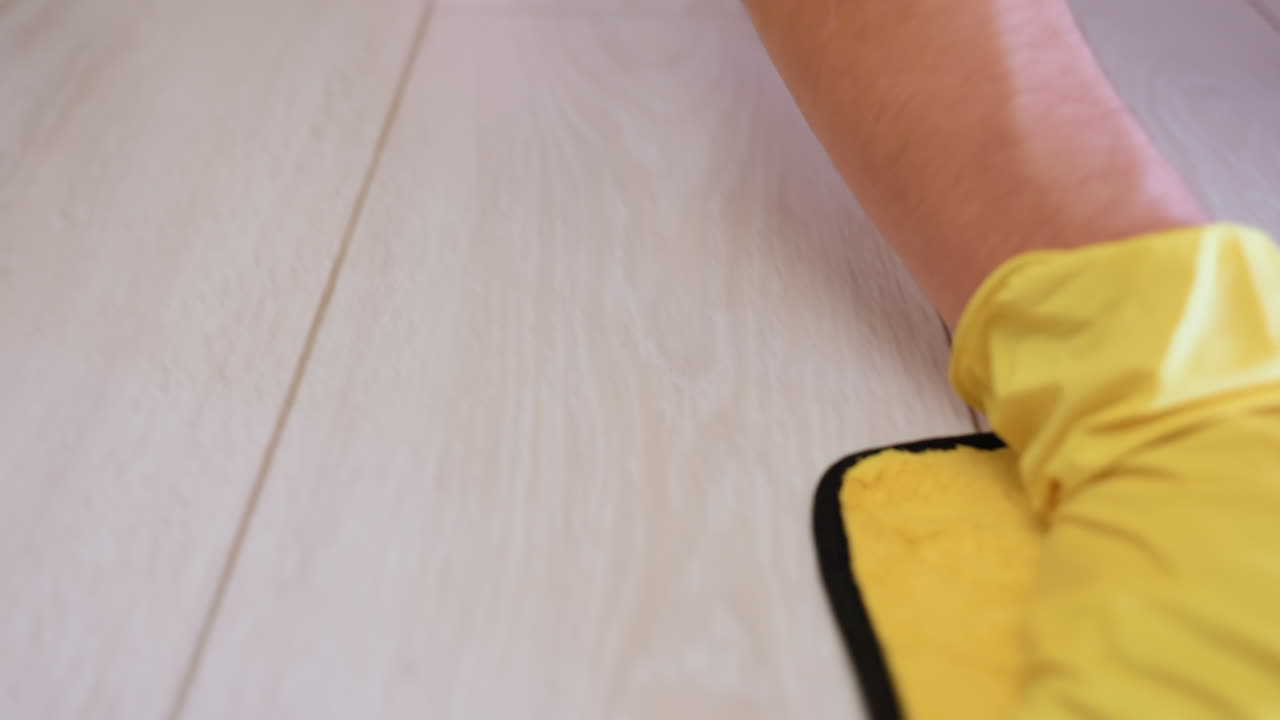 Close up of person wearing yellow gloves pressing wet rag on wooden floor, showing household cleaning process with sanitation, hygiene, manual work and detail of domestic maintenance