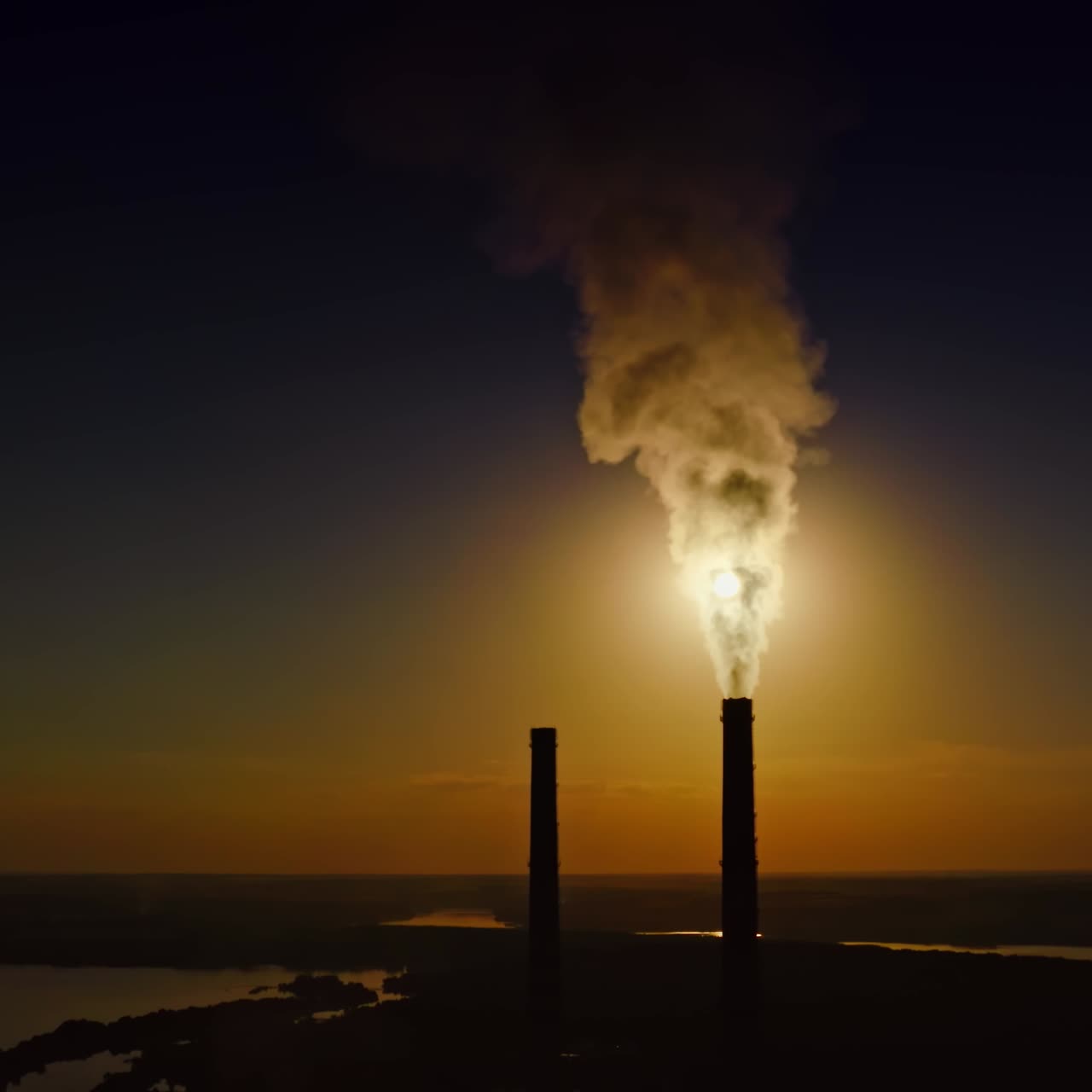 Dense smoke from pipes at sunset. Massive fumes released from industrial chimney into the environment. Nature in danger.