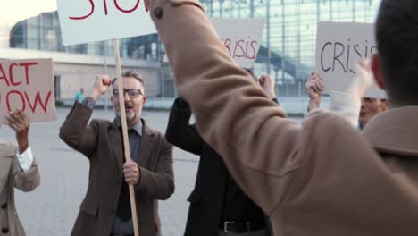 close-up view of caucasian man with glasses talking on the speaker with arms up in a protest with multiethnic business colleagues in the street