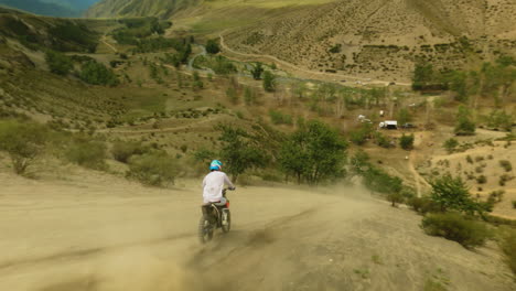 motorcyclist rides machine along dust hilly trail fpv. professional sportsman maneuvers modern motorcycle at highland. conquering wilderness