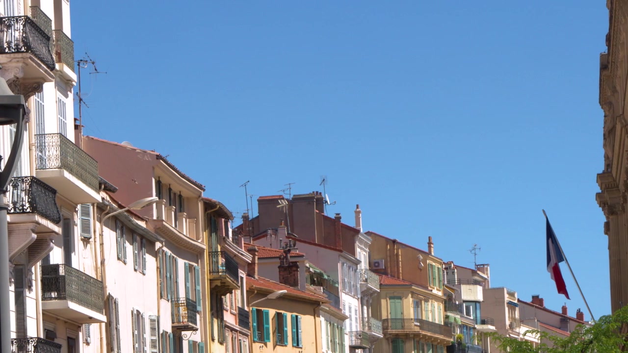 Carrellata di palazzi storici con persiane sotto un cielo estivo limpido e azzurro.