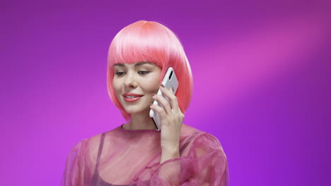 Cheerful-Woman-Wearing-A-Pink-Wig-And-Stylish-Outfit-Talking-On-Mobile-Phone-And-Smiling