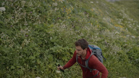 A-young-hiker-with-red-jacket-and-a-grey-backpack-walks-on-a-path-towards-the-top-of-mountain-Črna-prst-where-a-mountain-cottage-is-with-benches-outside-to-sit