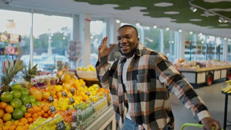 Portrait-of-a-Happy-man-with-Black-skin-color-in-a-plaid-shirt-and-a-white-T-shirt-who-is-happy-and-dancing-in-a-grocery-store-holding-a-grocery-basket-in-his-hands