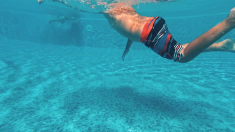young guy swims underwater in a swimming pool