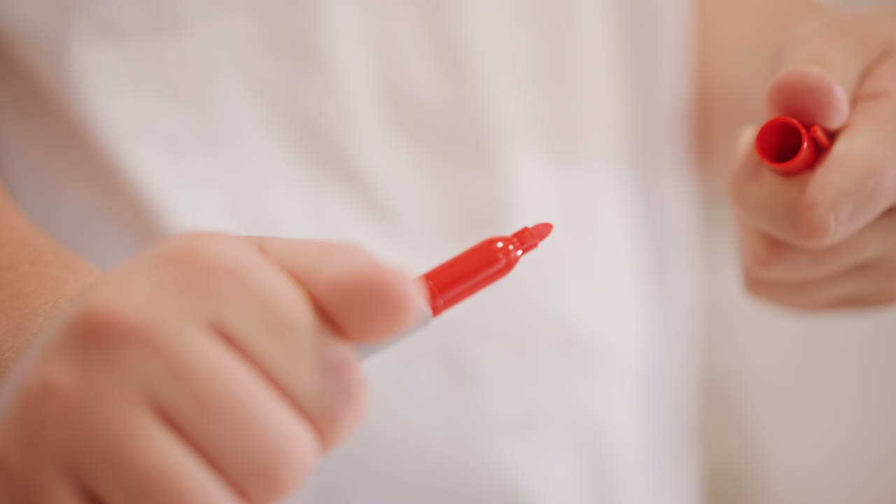 Detail dětských rukou otáčejících uzávěr fixu, malé prsty manipulující s plastovým uzávěrem s otáčivým tahem, hmatové zaměření na úchop a pohyb, běžné domácí osvětlení, upřímná studie zručnosti před vybarvováním.