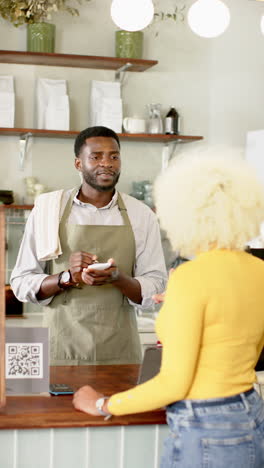 vertical video: barista taking order from customer in cafe, holding notepad and pen