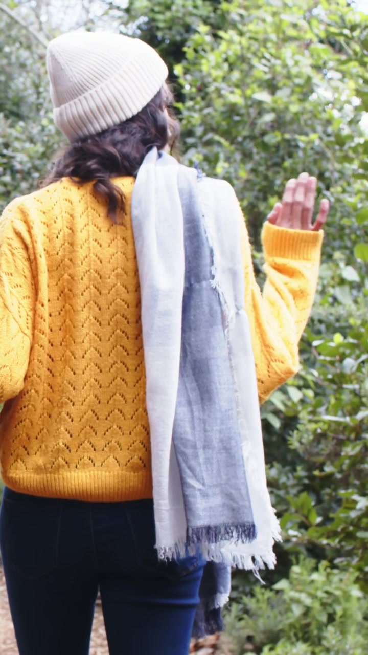 Vídeo vertical: Mulher caminhando usando cachecol de suéter amarelo, seguindo amiga por um caminho, com espaço para texto